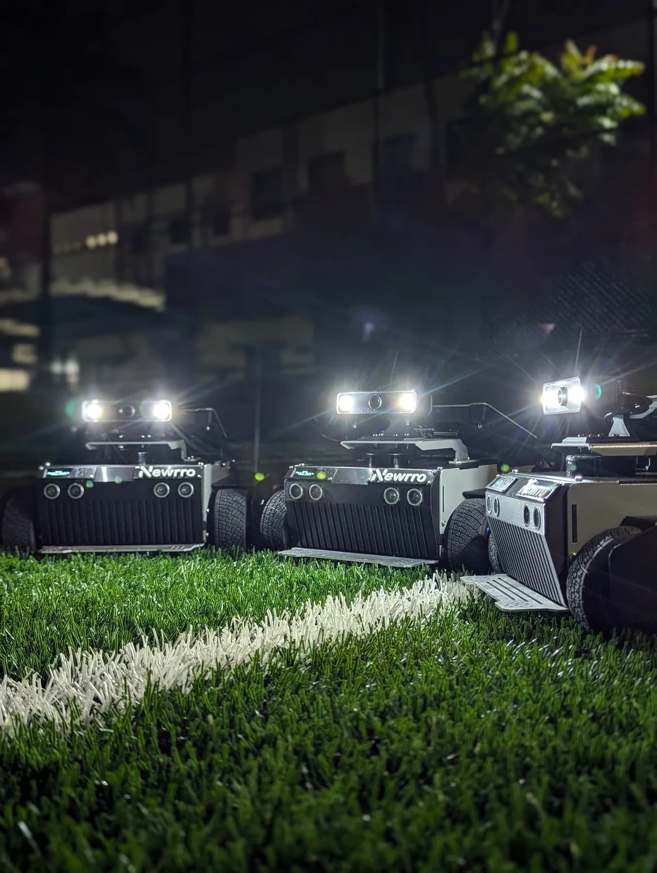 Three ARJUNA robots with headlights on, on turf at night